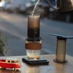 Aeropress coffee maker in use with a glass mug, scale, and kettle, illustrating useful Aeropress accessories for home brewers.