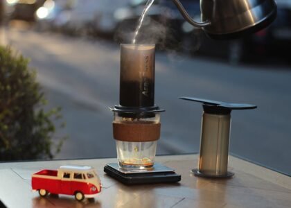 Aeropress coffee maker in use with a glass mug, scale, and kettle, illustrating useful Aeropress accessories for home brewers.