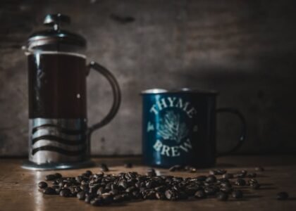 A cozy scene featuring a French press, a mug labeled 'Thyme for Brew', and coffee beans on a wooden table.