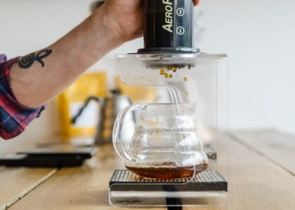 A person uses an AeroPress to brew espresso-style coffee into a glass carafe, illustrating the AeroPress vs French Press comparison.
