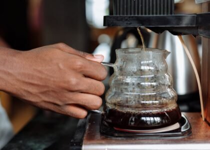 Person brewing coffee with an automatic drip coffee maker, showing a hand holding a glass carafe as coffee drips in.