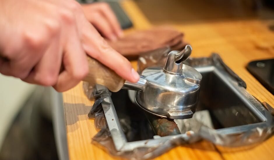 Close-up of a hand knocking used espresso grounds from a portafilter into a metal coffee knock box on a wooden counter.