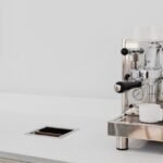 Sleek stainless steel espresso machine with cups in a bright kitchen setting.