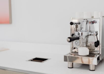 Sleek stainless steel espresso machine with cups in a bright kitchen setting.
