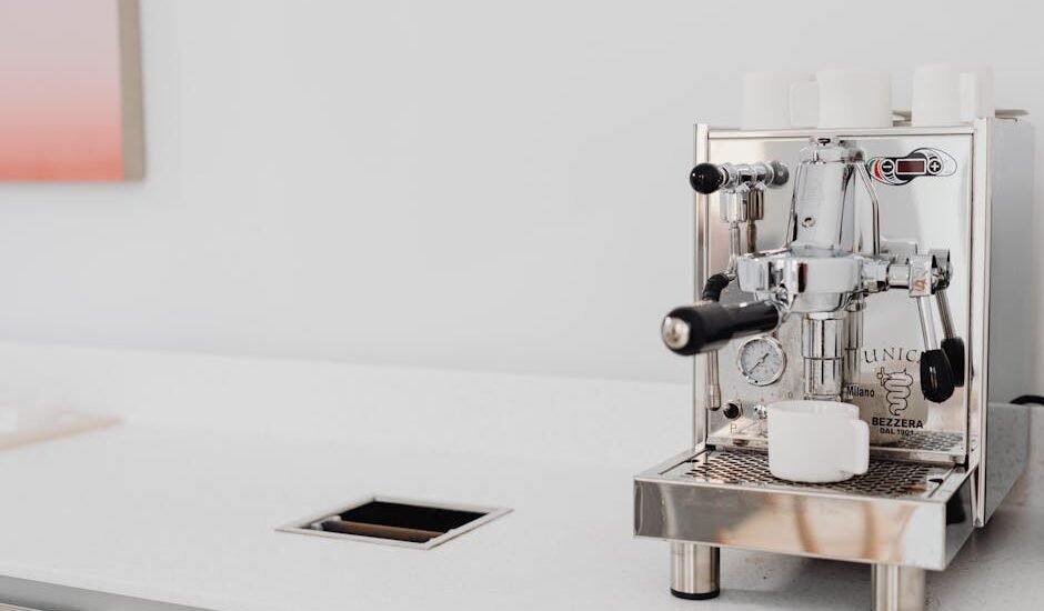 Sleek stainless steel espresso machine with cups in a bright kitchen setting.