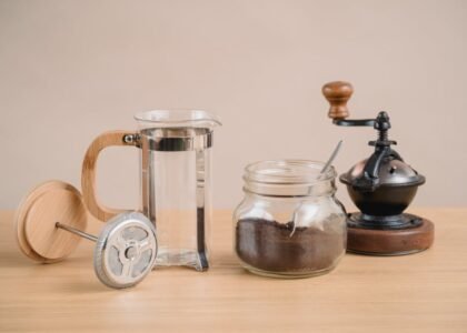 French press coffee gear including a manual grinder, glass jar of grounds, and empty press, illustrating grinder choices.