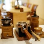 Selection of home barista accessories including manual coffee grinders, a tamper, and a portafilter on a kitchen counter.