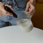 Person using a handheld milk frother to foam milk in a glass measuring cup, illustrating latte preparation for a milk frother guide