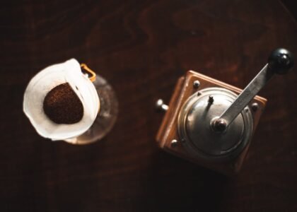 Coffee grinder retention explained with an overhead view of a manual grinder next to ground coffee in a paper filter.