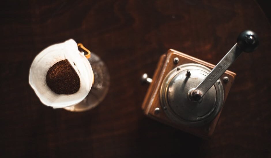 Coffee grinder retention explained with an overhead view of a manual grinder next to ground coffee in a paper filter.