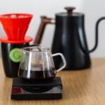 Close-up of a V60 coffee setup with dripper, scale, and kettle, highlighting specialty coffee brewing.