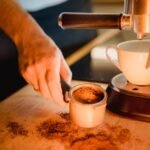 Close-up of a person loading ground coffee into a portafilter next to an espresso machine, highlighting water filter use.