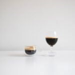Two espresso shot glasses, one small and one larger, filled with espresso, relevant to espresso shot glasses for machines.