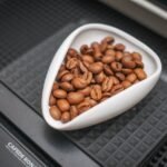 Digital coffee scale with a white dish of whole coffee beans, illustrating the calibration process for accurate brewing.