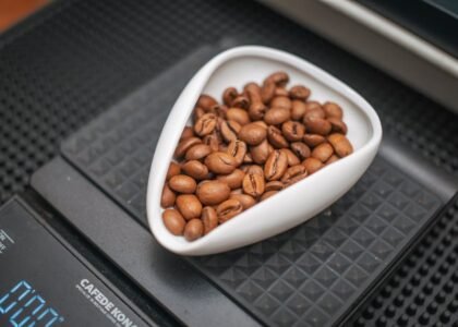 Digital coffee scale with a white dish of whole coffee beans, illustrating the calibration process for accurate brewing.