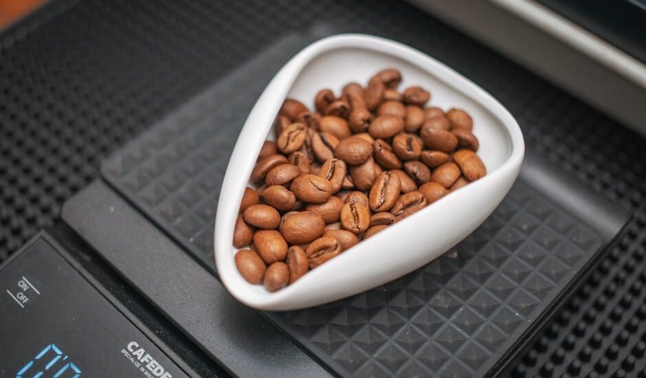 Digital coffee scale with a white dish of whole coffee beans, illustrating the calibration process for accurate brewing.