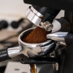 Close-up of an espresso grinder dispensing ground coffee into a portafilter, illustrating grind size adjustment for espresso preparation.