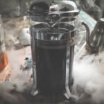A steaming French press filled with coffee sits on a kitchen counter, illustrating how to preheat a French press for better coffee.