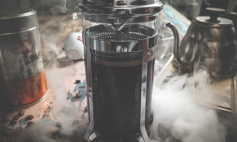 A steaming French press filled with coffee sits on a kitchen counter, illustrating how to preheat a French press for better coffee.