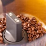 Whole coffee beans inside a new grinder hopper, illustrating the first step in seasoning a coffee grinder
