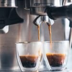 Close-up of espresso machine brewing two shots into glass cups, illustrating brew chamber age comparison topic