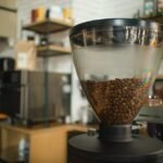 A single dose coffee grinder with a large transparent hopper filled with beans, illustrating grinder features for buyers