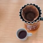 Reusable coffee filter with used grounds in a pour-over dripper beside a mug of brewed coffee, illustrating filter options.