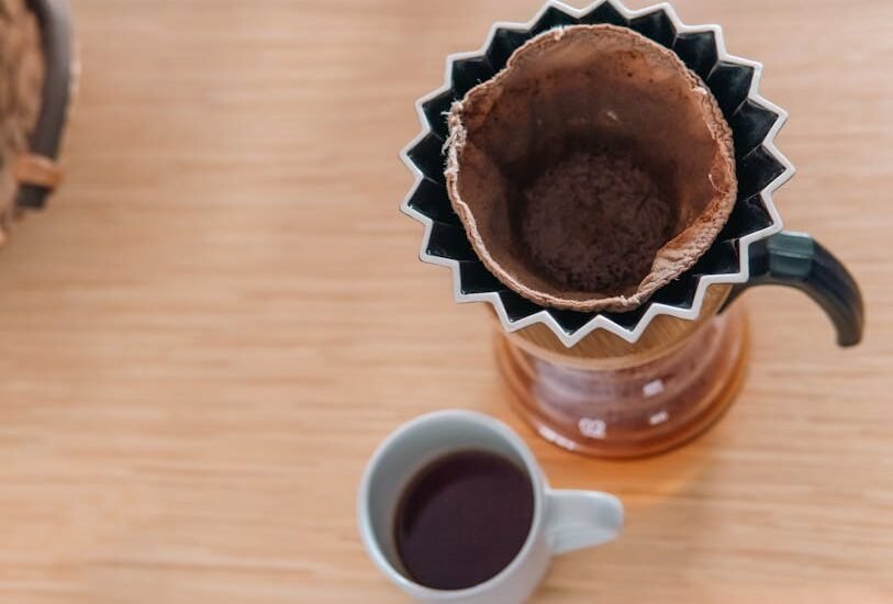 Reusable coffee filter with used grounds in a pour-over dripper beside a mug of brewed coffee, illustrating filter options.