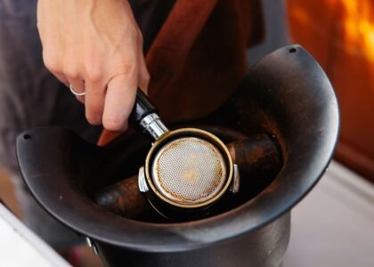 A hand knocks used espresso grounds from a portafilter into a coffee knockout box, illustrating its practical use.