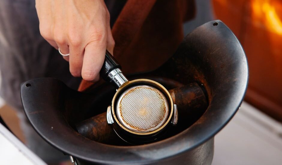 A hand knocks used espresso grounds from a portafilter into a coffee knockout box, illustrating its practical use.