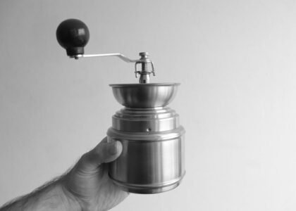 A hand holding a manual conical burr grinder, relevant for drip coffee brewing.