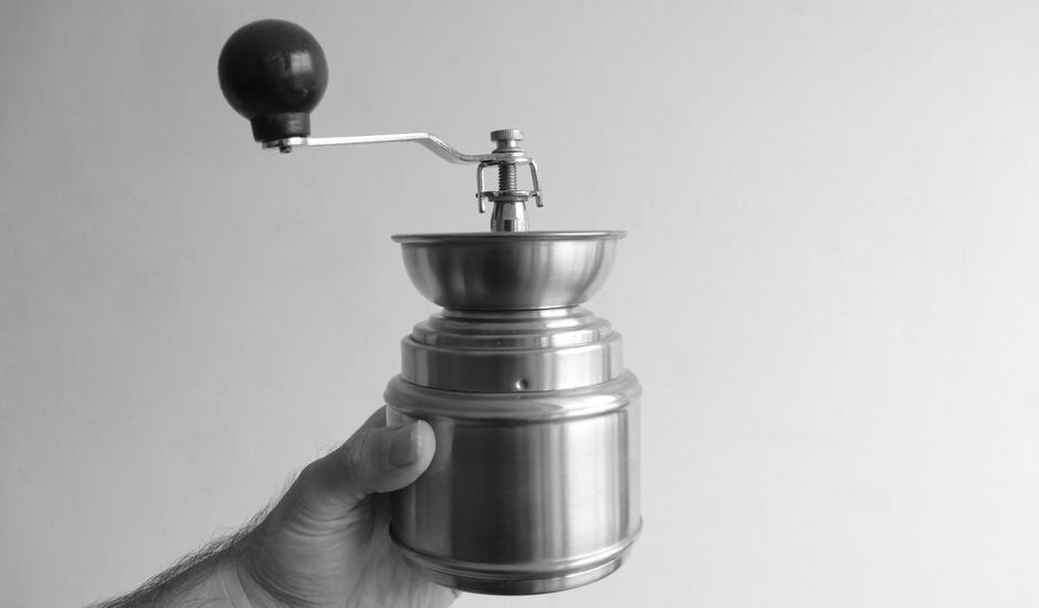 A hand holding a manual conical burr grinder, relevant for drip coffee brewing.