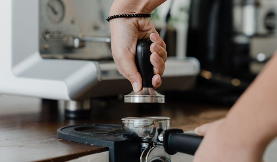 A hand using a tamper on an espresso tamping mat, illustrating the article on tamping mats.