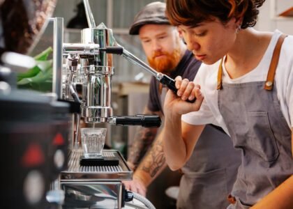A person operating a manual espresso lever machine while another observes, illustrating the article on manual espresso levers.