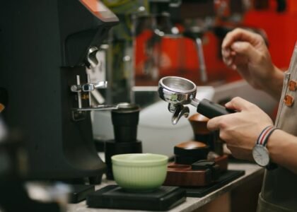 A person holds a portafilter near a coffee dosing cup while preparing espresso.