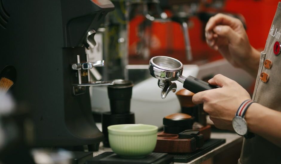 A person holds a portafilter near a coffee dosing cup while preparing espresso.