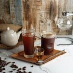 Cold brew maker setup featuring two glasses of cold brew coffee and coffee beans.
