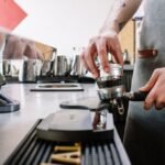 A person demonstrating the use of an espresso distribution tool on a portafilter.