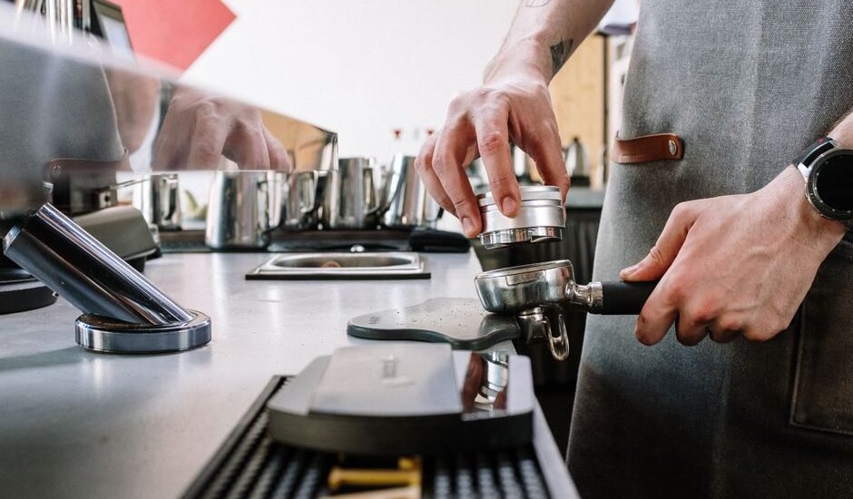 A person demonstrating the use of an espresso distribution tool on a portafilter.