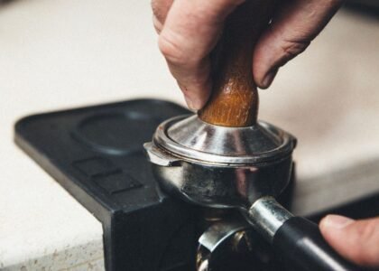 A hand pressing down on an espresso tamper with a wooden handle on a portafilter.