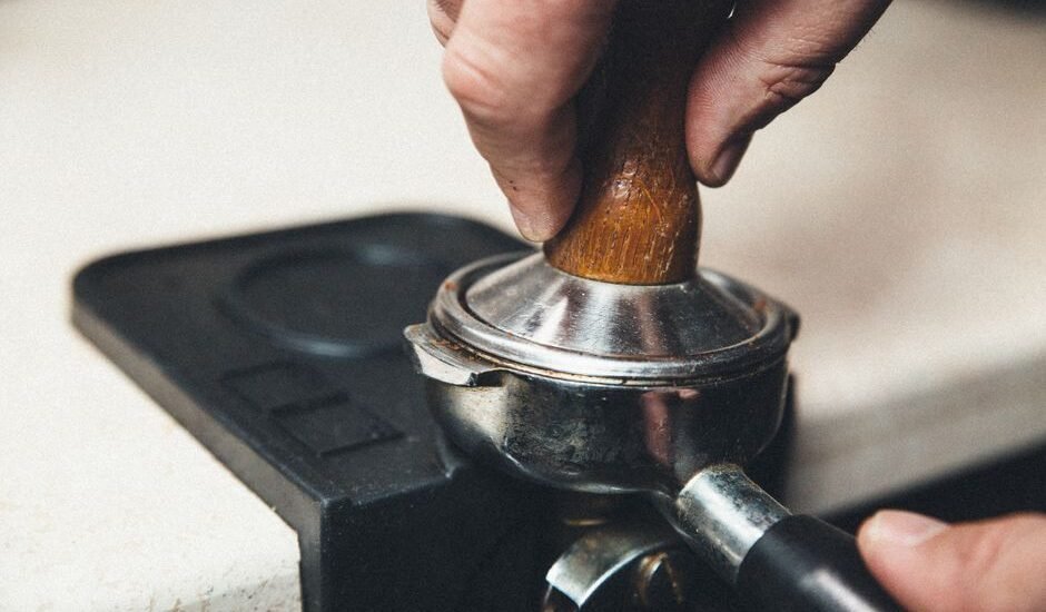 A hand pressing down on an espresso tamper with a wooden handle on a portafilter.