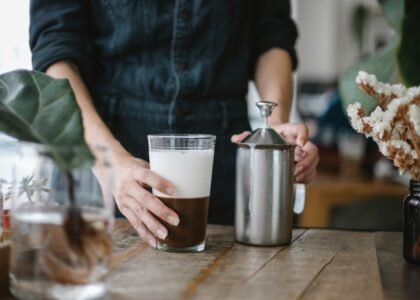 A person holding a glass of frothed milk next to a manual milk frother, illustrating how it works.