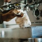 A hand holding a cloth while cleaning an espresso machine, related to descaling.