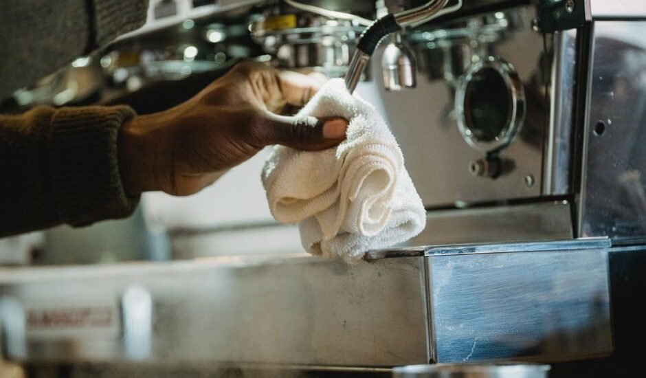 A hand holding a cloth while cleaning an espresso machine, related to descaling.