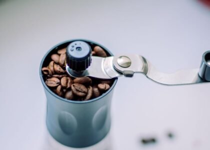 A hand grinder filled with coffee beans, illustrating disassembly steps.