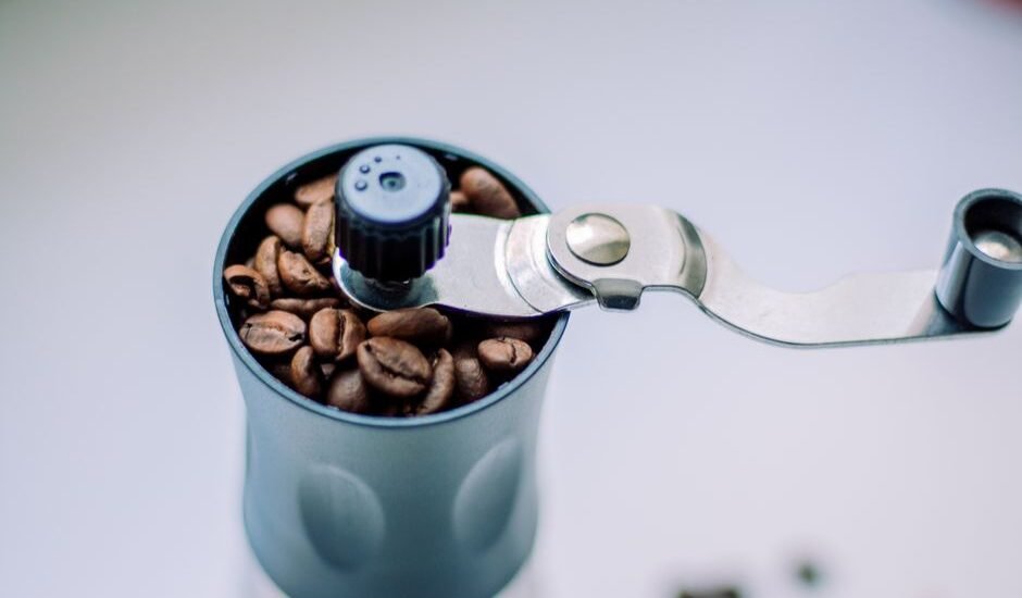 A hand grinder filled with coffee beans, illustrating disassembly steps.