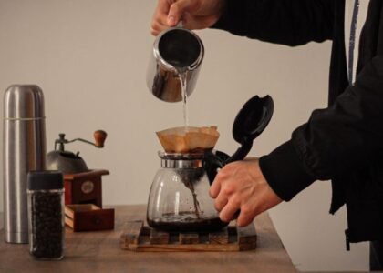 A person pours hot water over a coffee filter in a brewing setup, illustrating how to pre-wet a coffee filter.