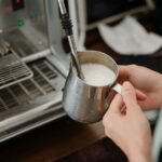 A person holding a metal milk pitcher while steaming milk with less foam.