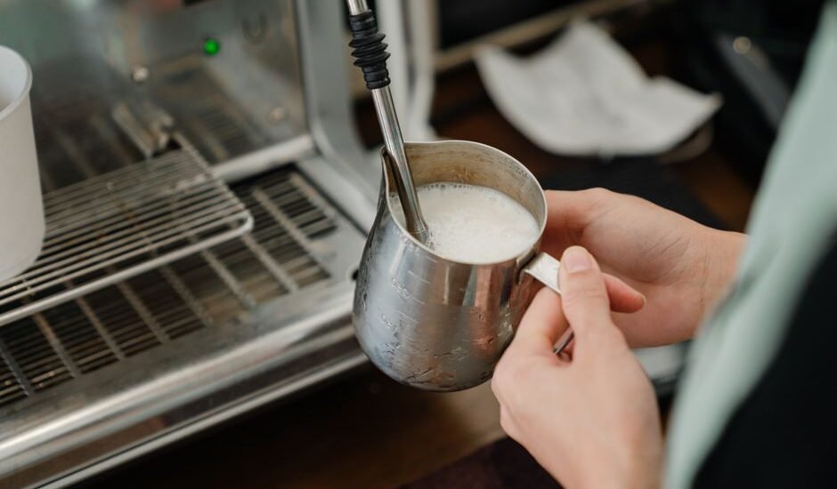 A person holding a metal milk pitcher while steaming milk with less foam.