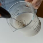 A person frothing milk in a measuring cup with a manual milk frother.